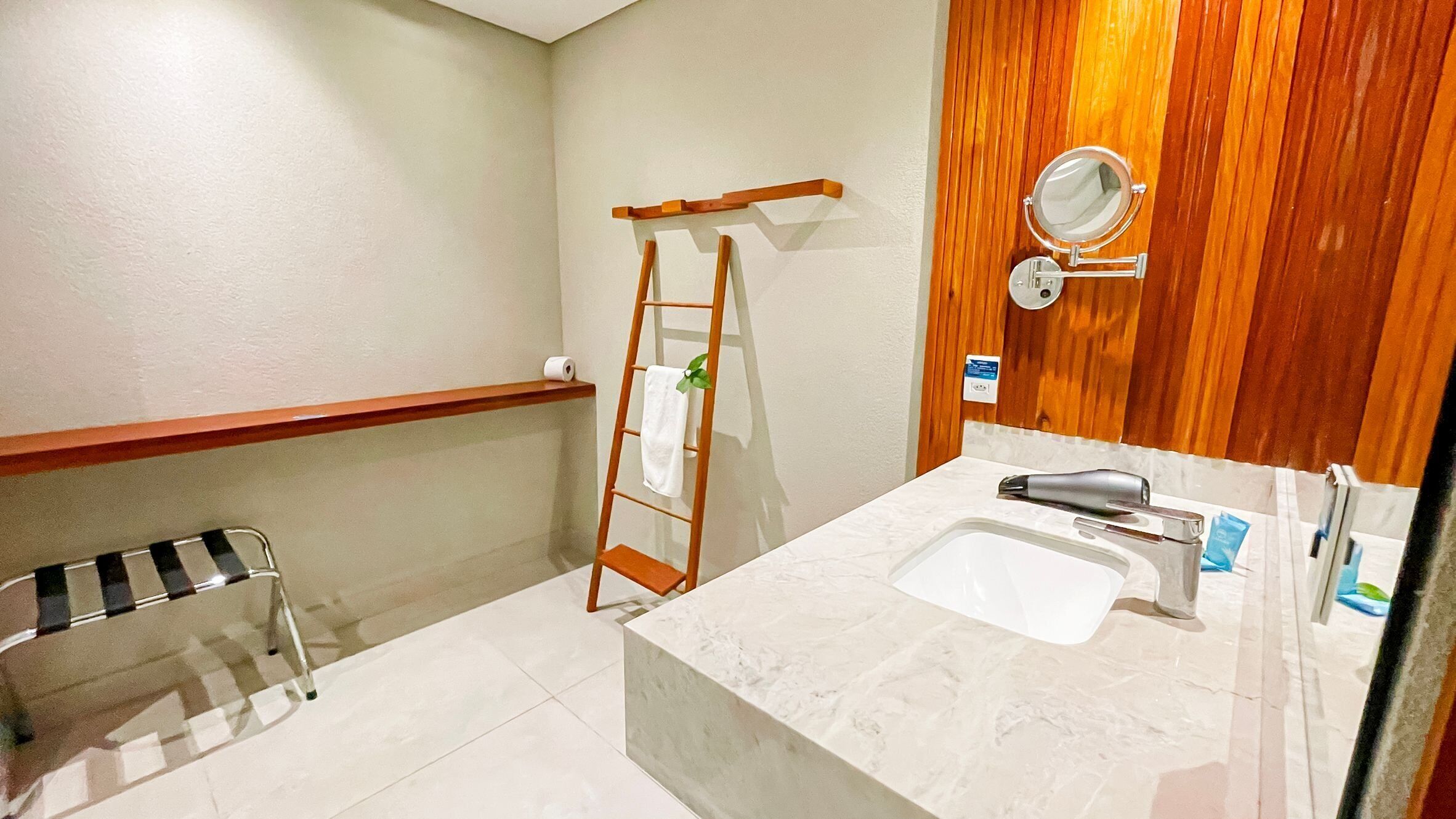 Un baño con una escalera de madera, un perchero, un lavabo con espejo y un dispensador de toallas.