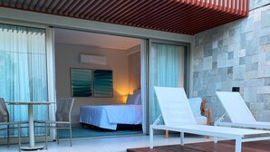 Een hotelkamer met een bed, twee witte fauteuils, een klein zwembad en uitzicht op de kamer via een glazen deur.