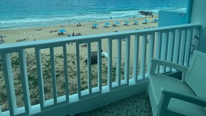 Varanda com vista para uma praia, com chão de azulejos e guarda-corpo branco.