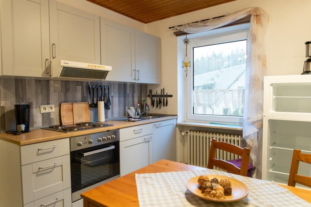 Une cuisine compacte avec des meubles blancs, une cuisinière, un four et une fenêtre donnant sur un paysage enneigé.