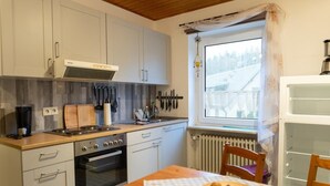 A compact kitchen with white cabinets, a stove, oven, and a window with a view of a snowy landscape.