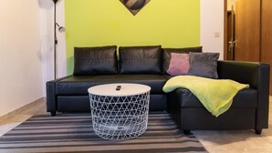 A modern living room with a black sofa, a geometric coffee table, and a green accent wall.