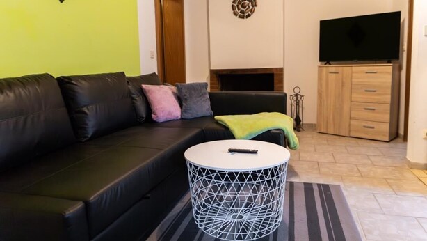 A living room with a black leather sofa, a white round coffee table, a television, and a fireplace.