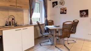 A kitchen with a dining table, wicker chairs, a window with curtains, and a wall clock. - Reiterhof Finkenmühle Fewo Gipsy (Weißenstadt)