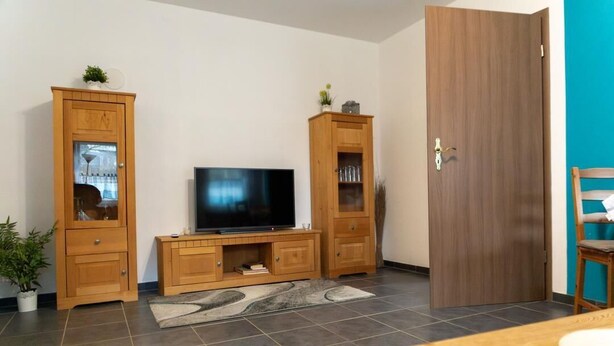Una sala de estar con televisor, armarios de madera, una puerta y una mesa.