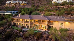 A two-story house with a pool, surrounded by rocky terrain and vegetation. - 8BR Exclusive Camelback Mansion w/ Mountain Views, Heated Pool, Spa & Theater (Phoenix)