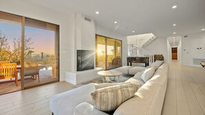 A modern living room with a large sofa, a coffee table, and a fireplace. There is a sliding glass door leading to an outdoor patio area. - 8BR Exclusive Camelback Mansion w/ Mountain Views, Heated Pool, Spa & Theater (Phoenix)