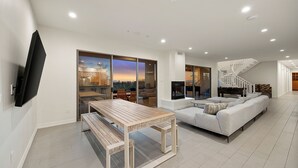 A modern living room with a flat-screen TV, a wooden dining table, a sofa, and a staircase. - 8BR Exclusive Camelback Mansion w/ Mountain Views, Heated Pool, Spa & Theater (Phoenix)