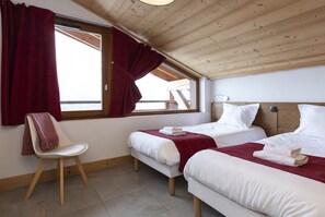 Een kamer met twee bedden, een stoel en een raam met gordijnen.