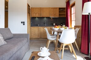 A modern kitchen with wooden cabinets, a dining table with chairs, and a sofa in the living area. - Residence Odalys Les Fermes De Chatel (Chatel)