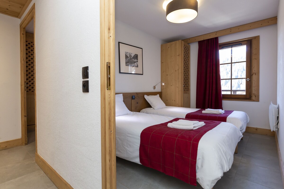 Una habitación con dos camas, cabecera de madera, ventana con cortina roja y un cuadro enmarcado en la pared.