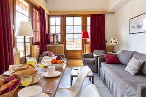 A cozy living room with a sofa, a dining table with breakfast items, and a view of mountains through large windows. - Residence Odalys Les Fermes De Chatel (Chatel)
