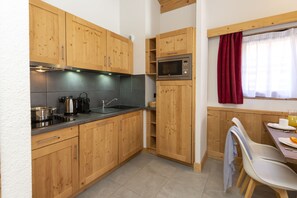 A kitchen with wooden cabinets, a microwave, and a dining area with a table and chairs. - Residence Odalys Les Fermes De Chatel (Chatel)