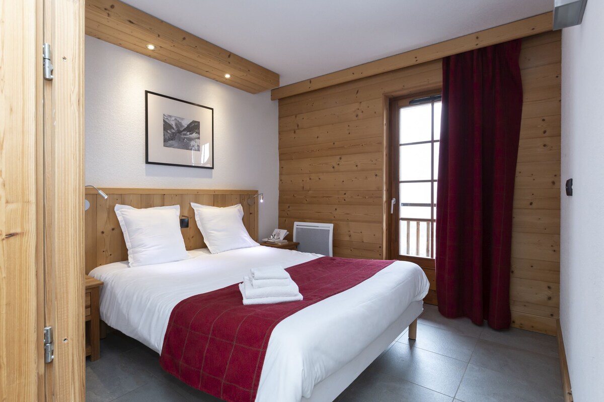 Una habitación con paneles de madera, una cama, un cuadro en la pared y una ventana con cortinas.