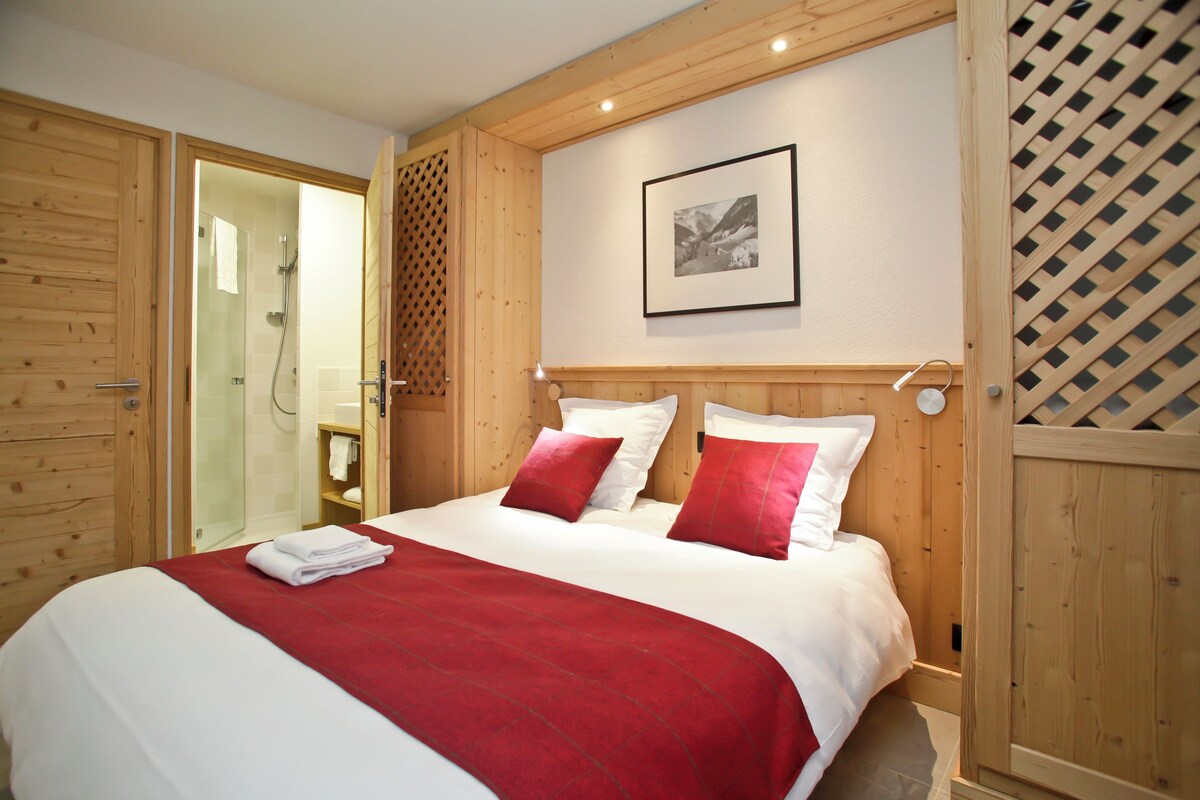 Habitación de hotel con una cama grande, paneles de madera, ducha y un cuadro enmarcado en la pared.
