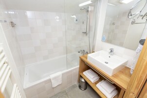 A modern bathroom with a glass-enclosed shower, a white bathtub, a wooden vanity with a sink, and a mirror.