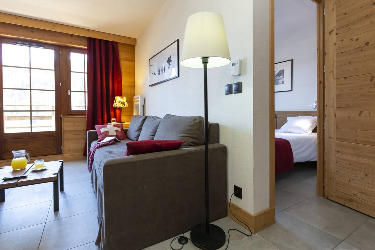A room with a sofa, a standing lamp, a bed, and a table with a pitcher of juice.
