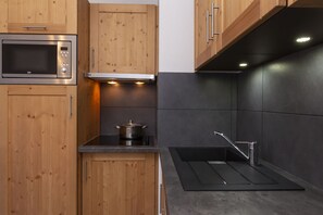 A modern kitchen with wooden cabinets, a built-in microwave, a stove, and a black countertop. - Residence Odalys Les Fermes De Chatel (Chatel)