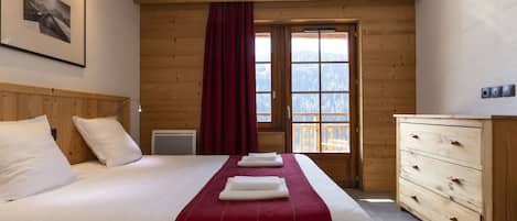 Habitación de hotel con cama, cómoda de madera, ventana con vistas y un cuadro en la pared.