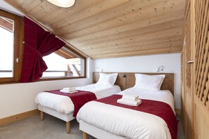 Una stanza con due letti, soffitto in legno e una finestra con tende rosse.