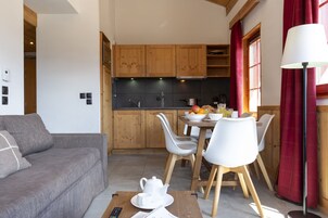 A modern kitchen with wooden cabinets, a dining table with chairs, and a sofa in a living area.