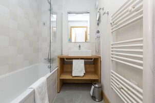 A bathroom with a bathtub, a sink, a mirror, a towel rack, a heater, and a trash bin.