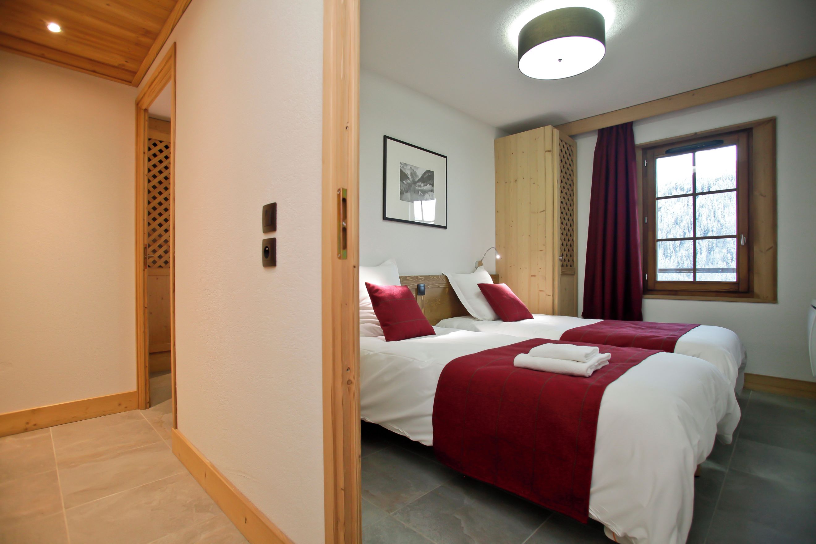 Una camera d'albergo con due letti, una finestra con tende, un quadro appeso al muro e una porta in legno.