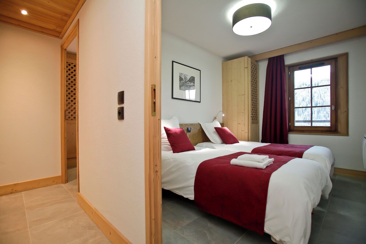 Una habitación de hotel con dos camas, un armario de madera, una ventana con cortinas, un cuadro enmarcado en la pared y una lámpara en el techo.