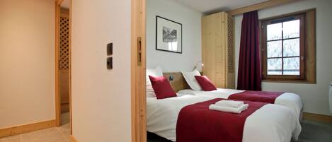 Una habitación de hotel con dos camas, una ventana con cortinas, un cuadro en la pared y una puerta de madera.
