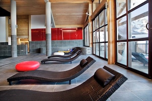 A spa area with reclining loungers, a red ottoman, and large windows offering a view of the mountains.