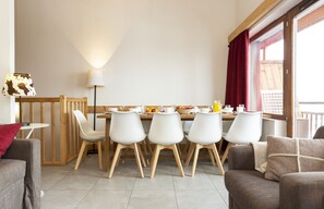 Un coin repas avec une table dressée pour quatre personnes, entourée de chaises blanches, d’une cloison en bois et d’une lampe.