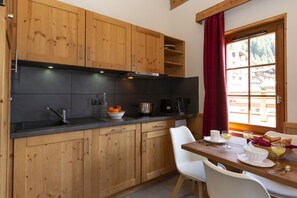 A kitchen with wooden cabinets, a black countertop, and a dining area with a table set for breakfast. - Residence Odalys Les Fermes De Chatel (Chatel)