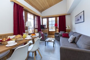 Una habitación con techo de madera, un sofá, una mesa de comedor con sillas, un televisor y una ventana con cortinas.