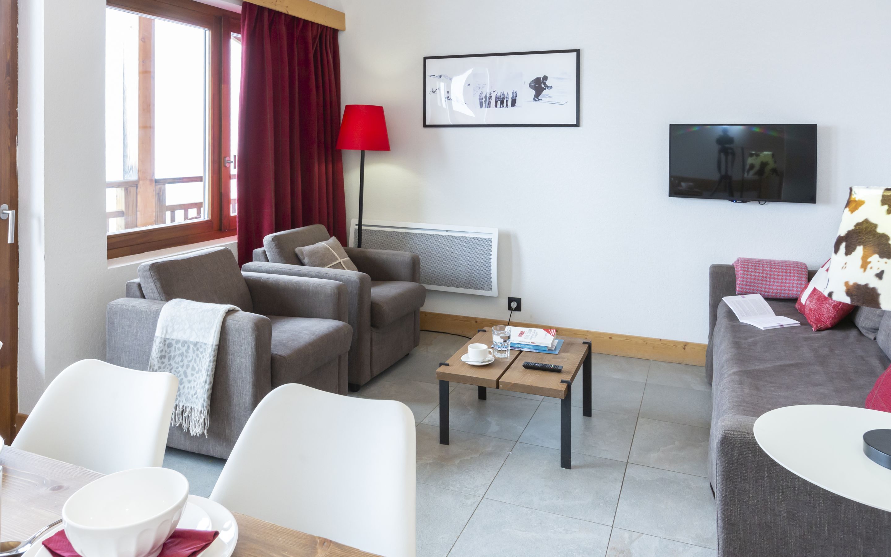 Un salon comprenant un canapé, des fauteuils, une table basse, un téléviseur et une fenêtre avec des rideaux.