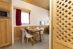 A wooden-paneled kitchen with a dining table, chairs, a microwave, and a window with curtains. - Residence Odalys Les Fermes De Chatel (Chatel)