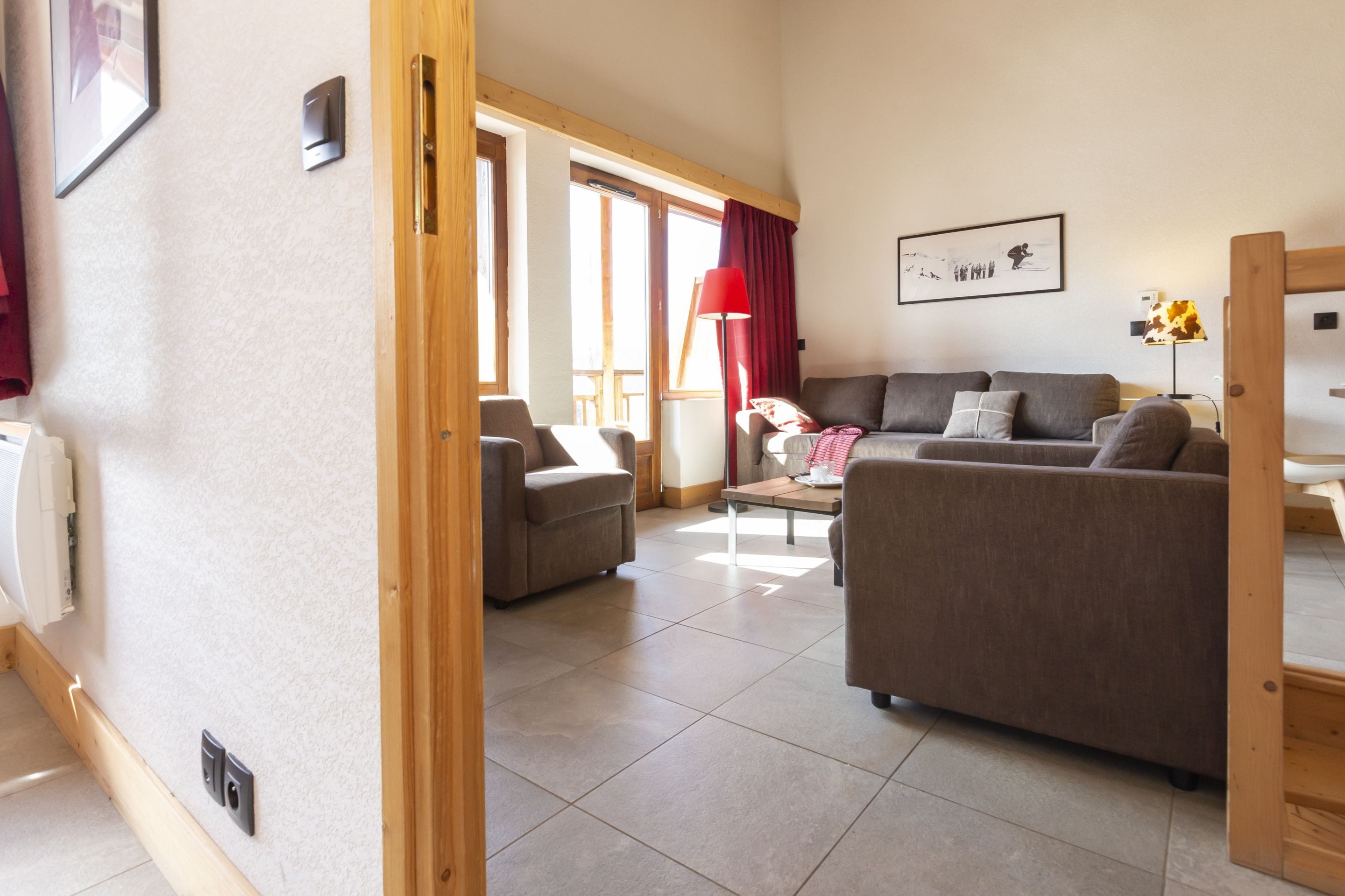 Un salon comprenant un canapé, un fauteuil et une table à manger. Il y a une fenêtre avec des rideaux, une lampe et un tableau encadré au mur.