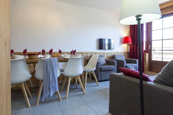Un coin repas avec une table dressée pour quatre personnes, un canapé, un téléviseur fixé au mur et une lampe.
