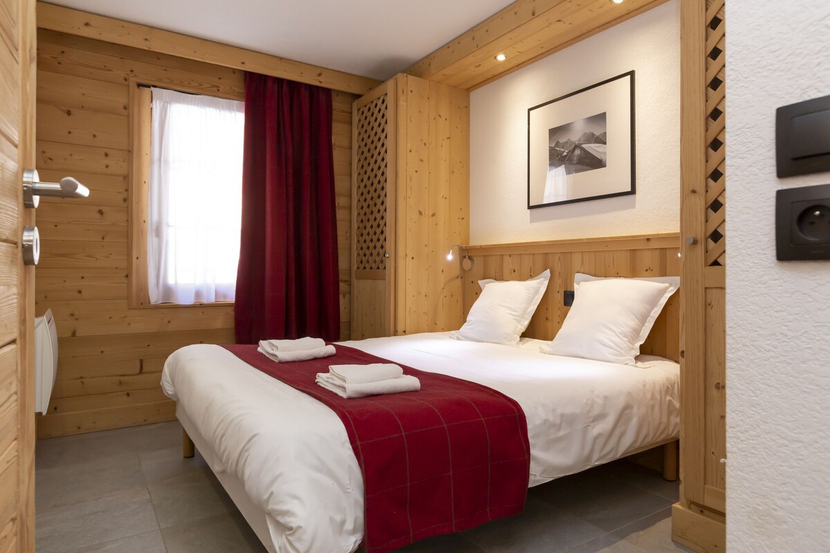 Una habitación con paneles de madera, una cama, una ventana con cortinas, un cuadro en la pared y un termostato.