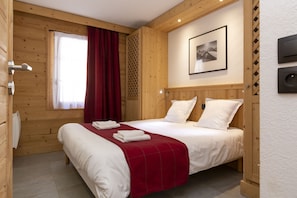 A wooden-paneled room with a bed, a window with curtains, a framed picture on the wall, and a thermostat. - Residence Odalys Les Fermes De Chatel (Chatel)