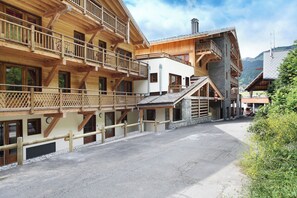 Un edificio de madera de varios pisos con balcones, fachada de piedra y un telesilla visible al fondo.