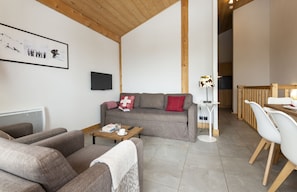 A living room with a sofa, a coffee table, a TV, and a dining area with chairs and a table. - Residence Odalys Les Fermes De Chatel (Chatel)