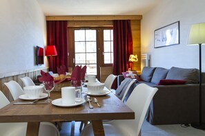 Een eethoek met een houten tafel voor vier personen, witte stoelen, een bank en een rode lamp.