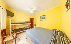 A room with a bunk bed, a single bed, a chair, a ceiling fan, and a painting on the wall.