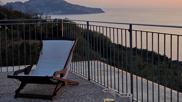 Una terraza con una mesa dispuesta para dos, con vistas a la costa y montañas al fondo.