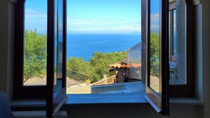 Una habitación con un ventanal grande que ofrece vistas al mar y al verdor.