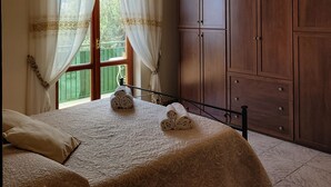 Un dormitorio con cama, mesita de noche, armario de madera y ventana con cortinas.
