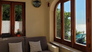 Una sala de estar con un sofá, una pequeña mesa de madera y ventanas amplias con vista al mar.