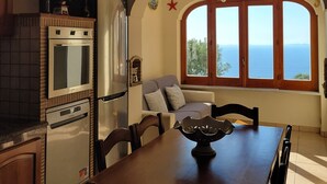 Una cocina con estufa, horno y refrigerador. Hay una mesa de comedor con sillas y una ventana con vista al mar.