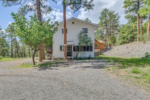 Una casa de dos pisos con camino de grava, rodeada de pinos.