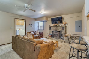 A living room with a fireplace, a ceiling fan, and a television mounted on the wall.